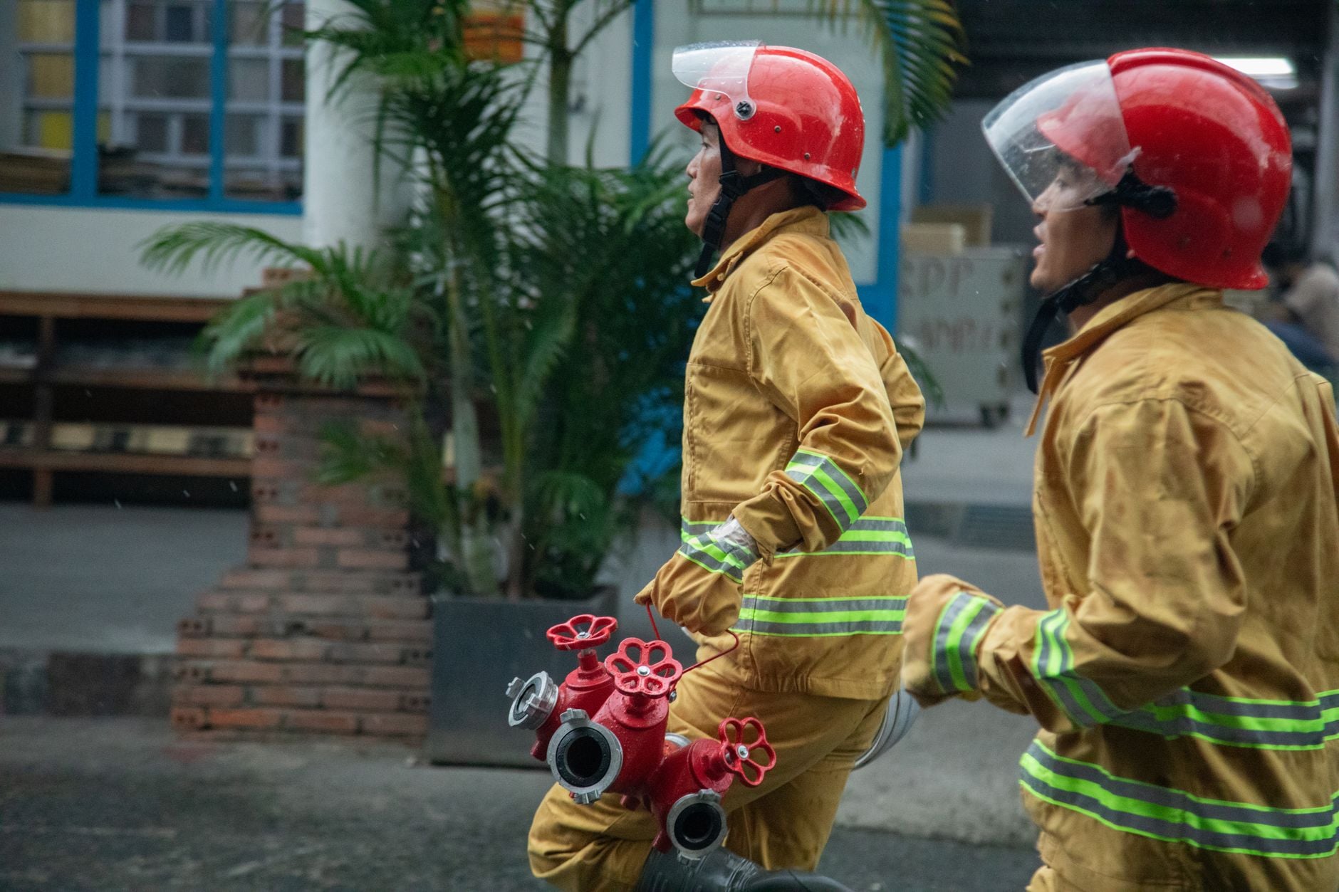 Two firefighters running with equipment through the city streets.