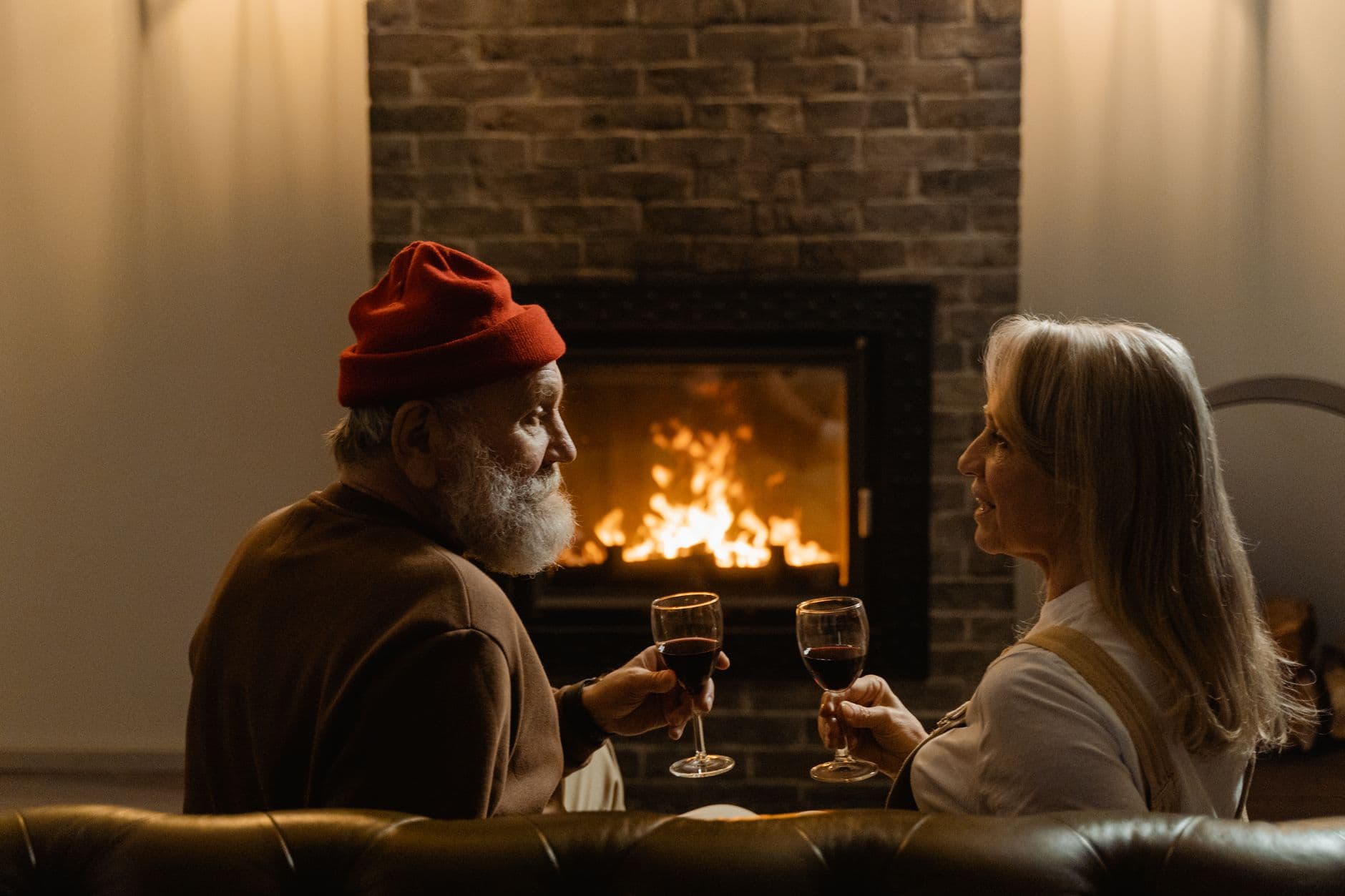 Charming scene of a senior couple sharing wine by a warm fireplace. Cozy and romantic.